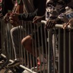 DHS Drops Bombshell: Asylum Work Permits Halted People leaning on barriers at an outdoor event