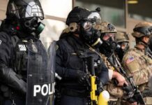 Police officers in tactical gear and gas masks standing in formation