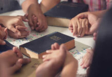 People holding hands with Bibles on table