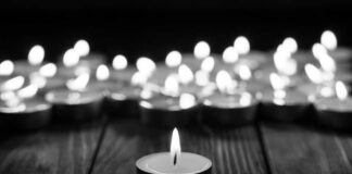 Single candle burning among many on wooden surface.