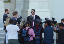 Group of reporters surrounding a man in sunglasses