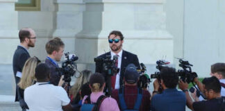 Group of reporters surrounding a man in sunglasses