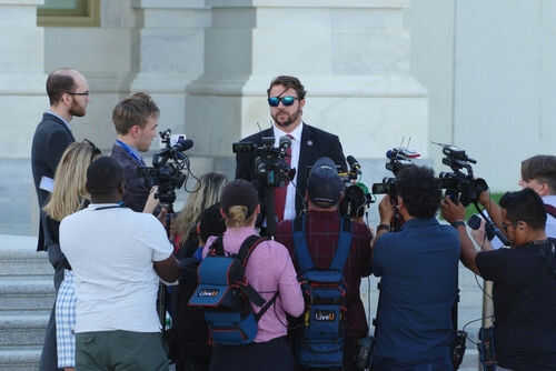 Group of reporters surrounding a man in sunglasses