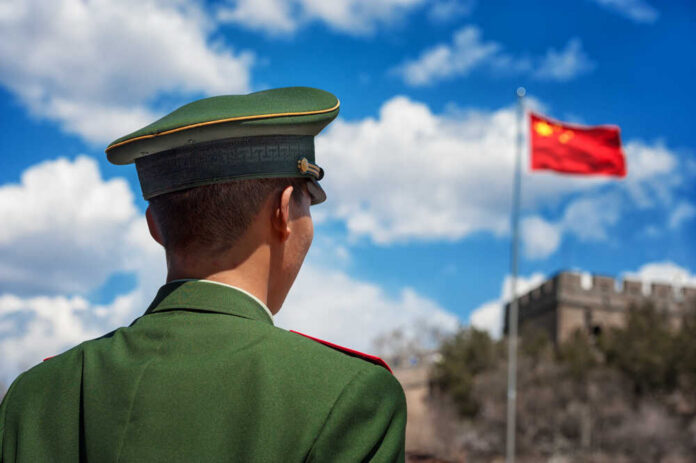 Soldier in a green military uniform facing the Great Wall of China with the Chinese flag in the background