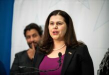 A woman in a black blazer speaking at a podium during a conference