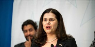 A woman in a black blazer speaking at a podium during a conference
