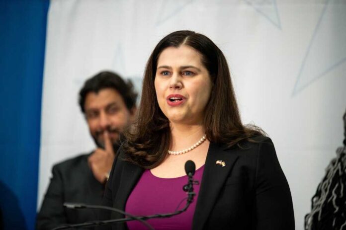A woman in a black blazer speaking at a podium during a conference