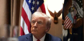 Man in suit sitting with flag background and eagle decoration