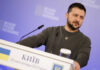 Zelensky’s Secret Gulf Deals: What’s Really Happening? man on podium