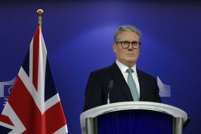 Man in suit at a podium, British flag behind.