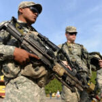 Soldiers in uniform holding weapons outdoors on sunny day