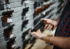 Person holding a handgun in a gun shop with various firearms displayed on the wall
