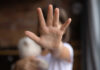 Child holding a teddy bear with a hand raised in a stop gesture