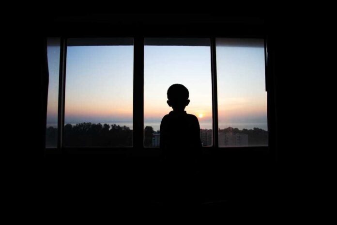 Silhouette of a child looking out a window at a sunset