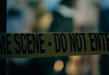 Caution tape marking a crime scene with blurred figures in the background