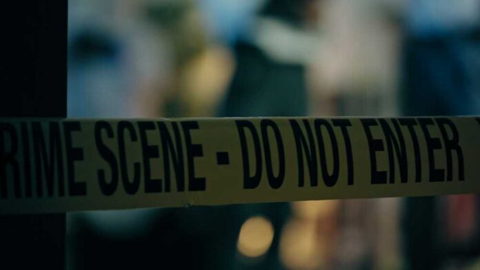 Caution tape marking a crime scene with blurred figures in the background