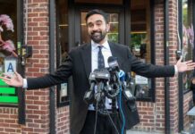 Man in a suit speaking at a press conference with microphones in front of him