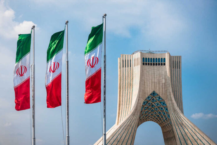 Three Iranian flags in front of the Azadi Tower against a blue sky
