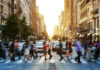 People crossing a busy city street at sunset