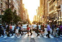 People crossing a busy city street at sunset
