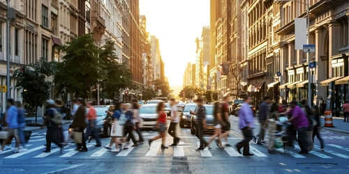 People crossing a busy city street at sunset