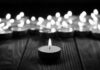 Single candle burning among many on wooden surface.