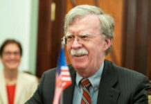 Man with glasses smiling near small American flag