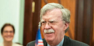 Man with glasses smiling near small American flag