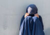 Disputed Rulings Fuel Pakistan Child Marriage Crisis Person in dark blue clothing sitting against a wall with face covered