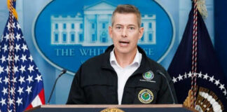 Man speaking at podium with presidential seal and flags