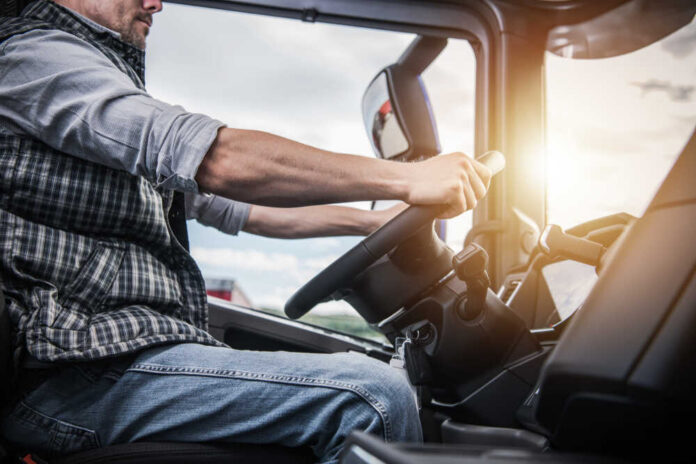 Truck,Driver,Behind,The,Wheel.,Semi,Truck,Driving,And,Transportation A truck driver gripping the steering wheel inside a vehicle cabin