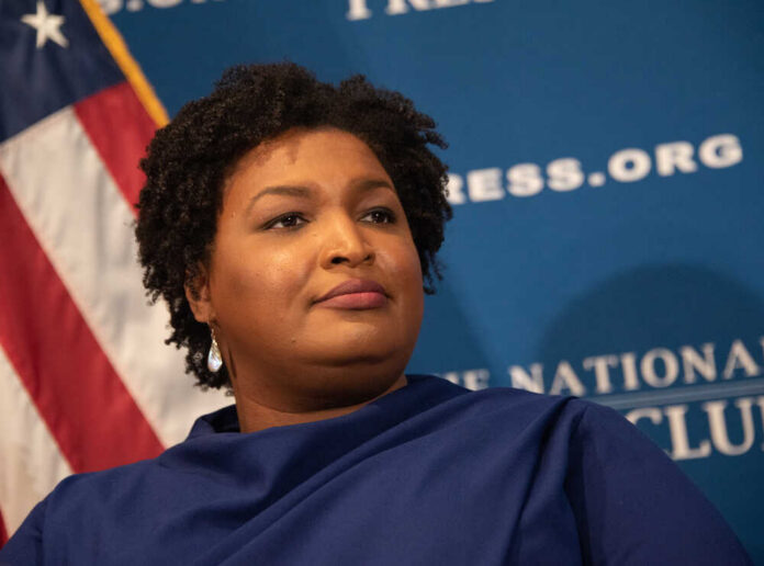 A woman with curly hair speaking at a podium in front of a blue backdrop