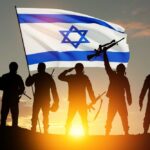 Silhouetted soldiers with rifles stand before an Israeli flag at sunset