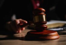 A wooden gavel resting on a table with a blurred hand in the background