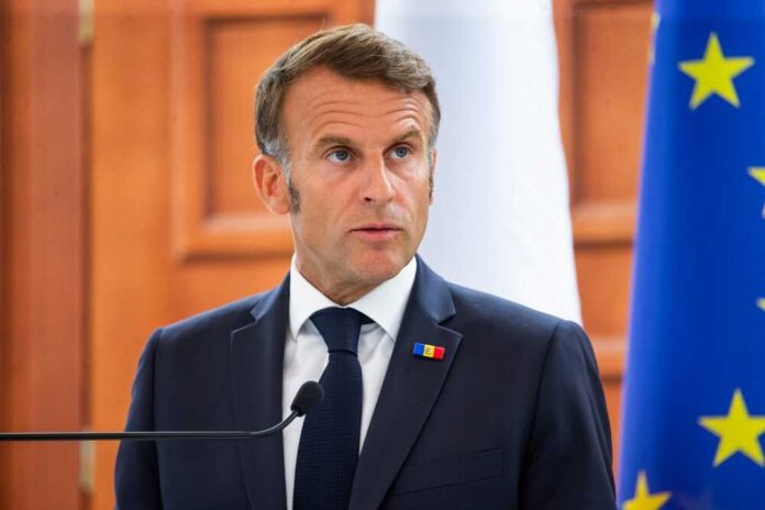 A political leader speaking at a press conference with flags in the background