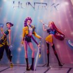 KPop Demon Hunters Tour Deception Exposed Three stylized female warriors on a display wall
