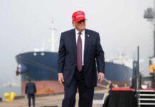Trump’s China Visit: Pageantry Over Progress? A man in a suit wearing a red cap stands near a ship at a harbor