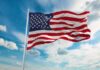 American flag waving on a flagpole against a blue sky with clouds