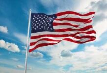 American flag waving on a flagpole against a blue sky with clouds