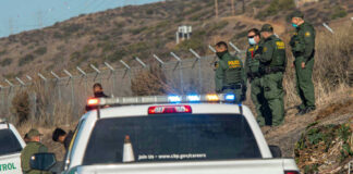 Border Patrol officers speaking with individuals near a fence.