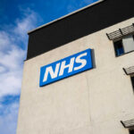 UK Eyes Break Clause to End Palantir NHS Deal NHS sign on modern hospital building exterior
