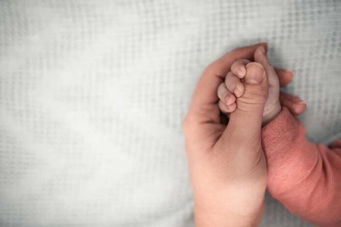 Welcome,Baby,mother,Holding,Her,Newborn,Baby,By,Little,Hand,,Love FDA paper with medical items on wooden table.