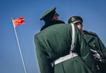 War Drills Or Siege? Taiwan Gets Squeezed Two Chinese soldiers in uniform standing near the national flag