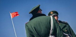 Two Chinese soldiers in uniform standing near the national flag