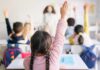 Students in a classroom raising their hands to answer a question