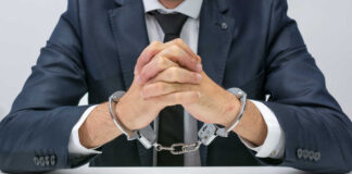 A man in a suit with hands handcuffed together on a table