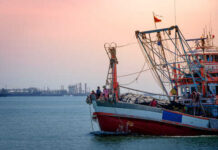 Fishing boat on the water during sunset with an industrial area in the background