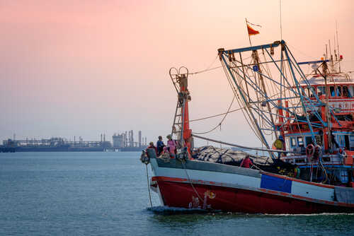 Fishing boat on the water during sunset with an industrial area in the background