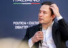 Probable Cause Hits Musk’s Cash-for-Votes Push Man in suit holding microphone at event indoors