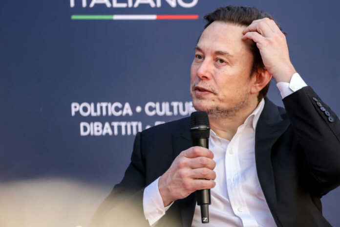 elon-musk2403657197jpg Man in suit holding microphone at event indoors